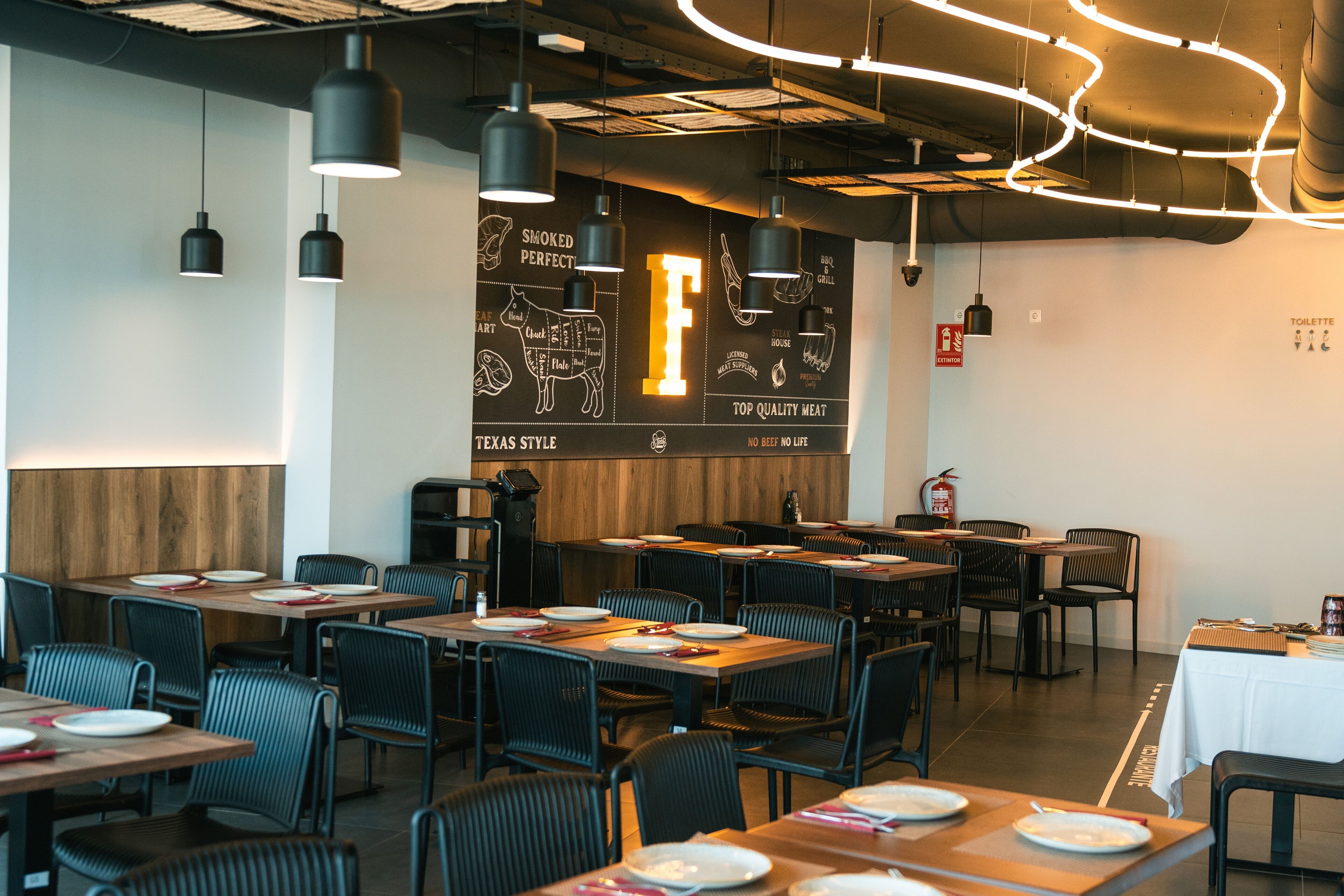 Interior de restaurante con varias mesas y sillas, una pared decorativa de madera y lámparas colgantes.