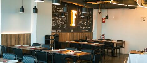 Interior de restaurante con varias mesas y sillas, una pared decorativa de madera y lámparas colgantes.