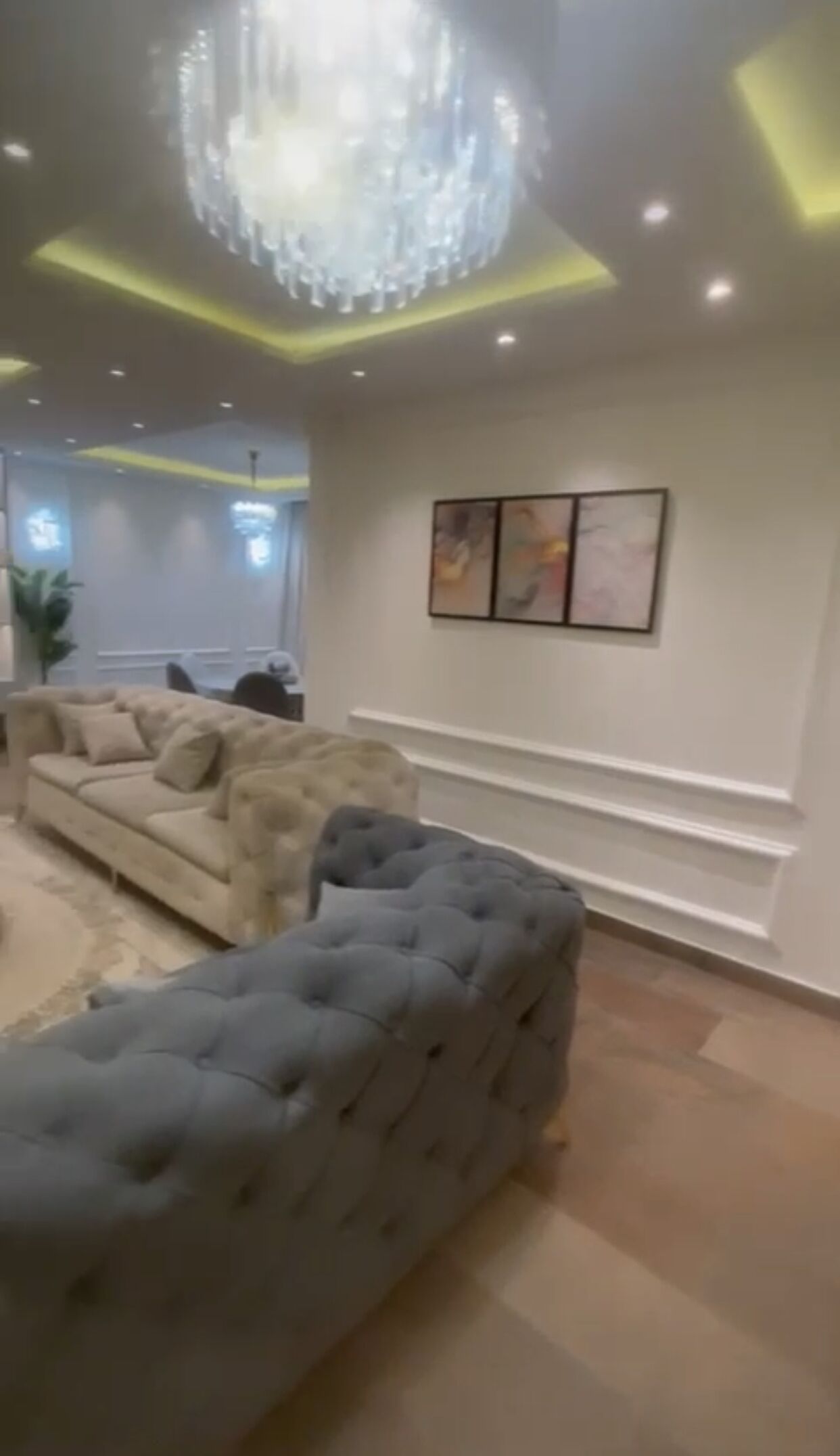 Un salon moderne doté d’un grand canapé d ’angle, d’un lustre, d’un éclairage encastré au plafond et d’une œuvre d’art accrochée au mur.