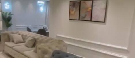 A modern living room with a large sectional sofa, a chandelier, recessed ceiling lighting, and a wall-mounted artwork.