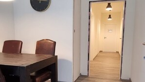 A hallway with a wooden floor, a dining area with a table and chairs, and a clock on the wall. - Zweibettzimmer in Zentraler Lage (Bremen)