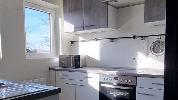 A modern kitchen with white cabinets, a built-in oven, and a microwave. - Zweibettzimmer in Zentraler Lage (Bremen)