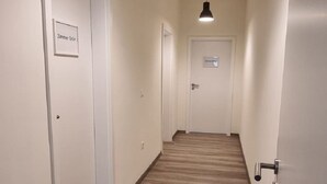 A hallway with wooden flooring, white walls, and black pendant lighting. - Zweibettzimmer in Zentraler Lage (Bremen)