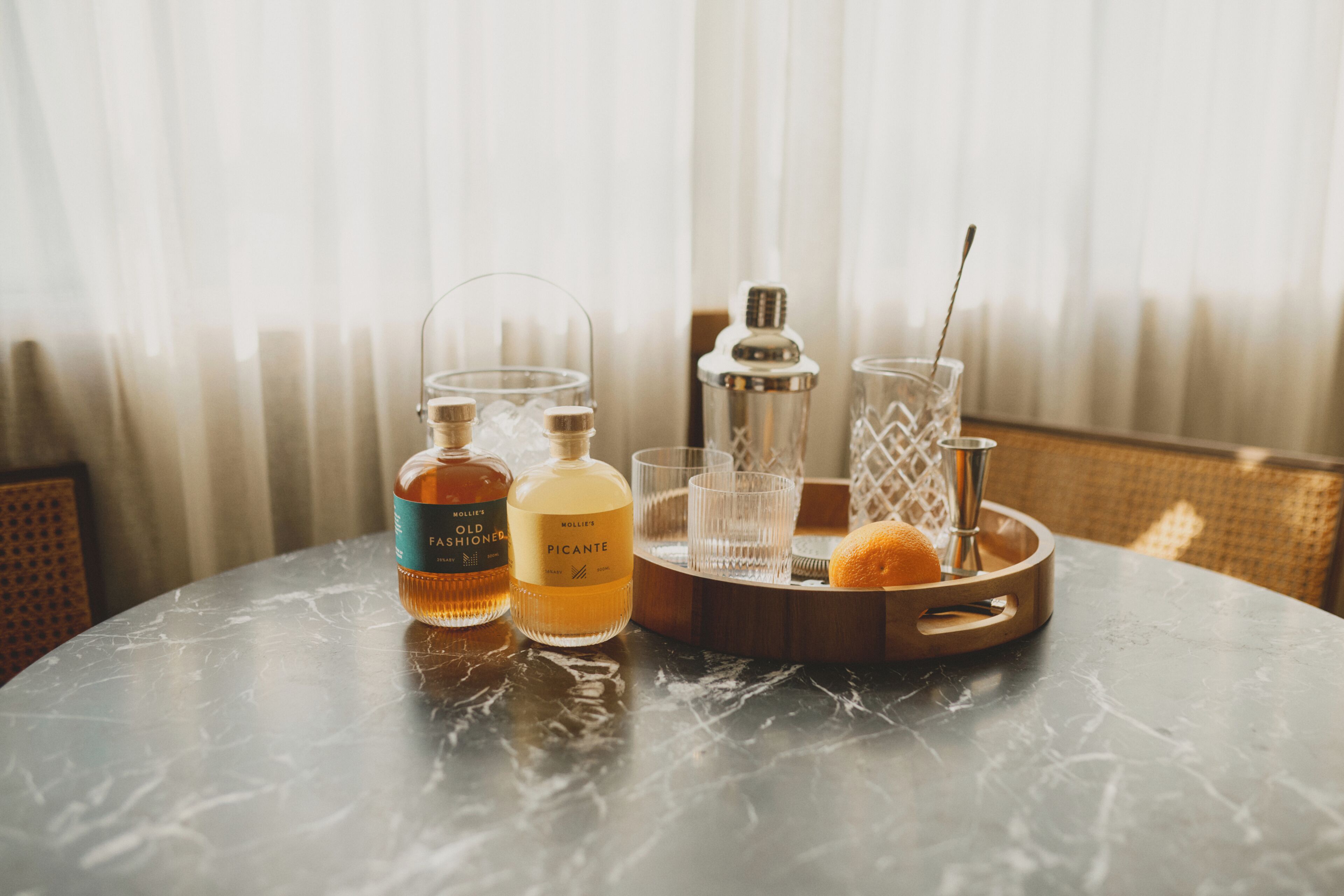 Een marmeren tafel met twee flessen, een glas en een houten dienblad met een metalen doseerder.