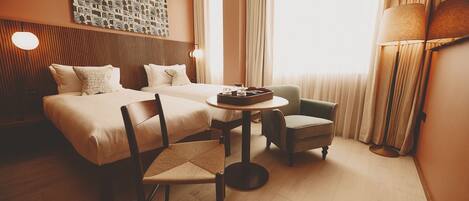 A hotel room with a bed, a chair, a small table with a tray, and a lamp.
