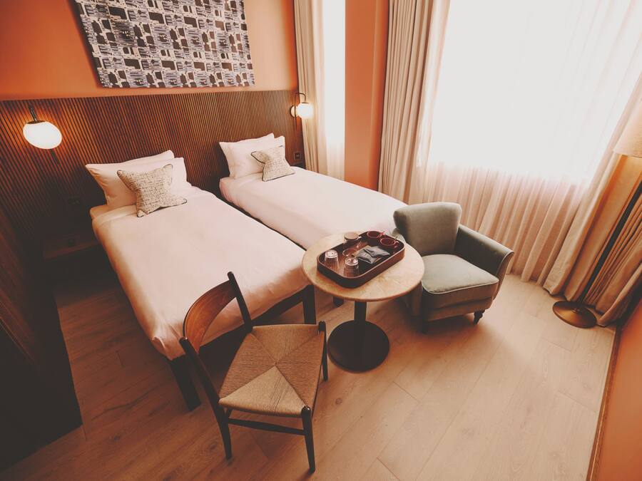 A hotel room with two beds, a small table with a tray, a chair, and a lamp.