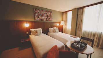 Una habitación de hotel con dos camas, una mesita con bandeja, una silla, una lámpara de pared y un adorno mural.