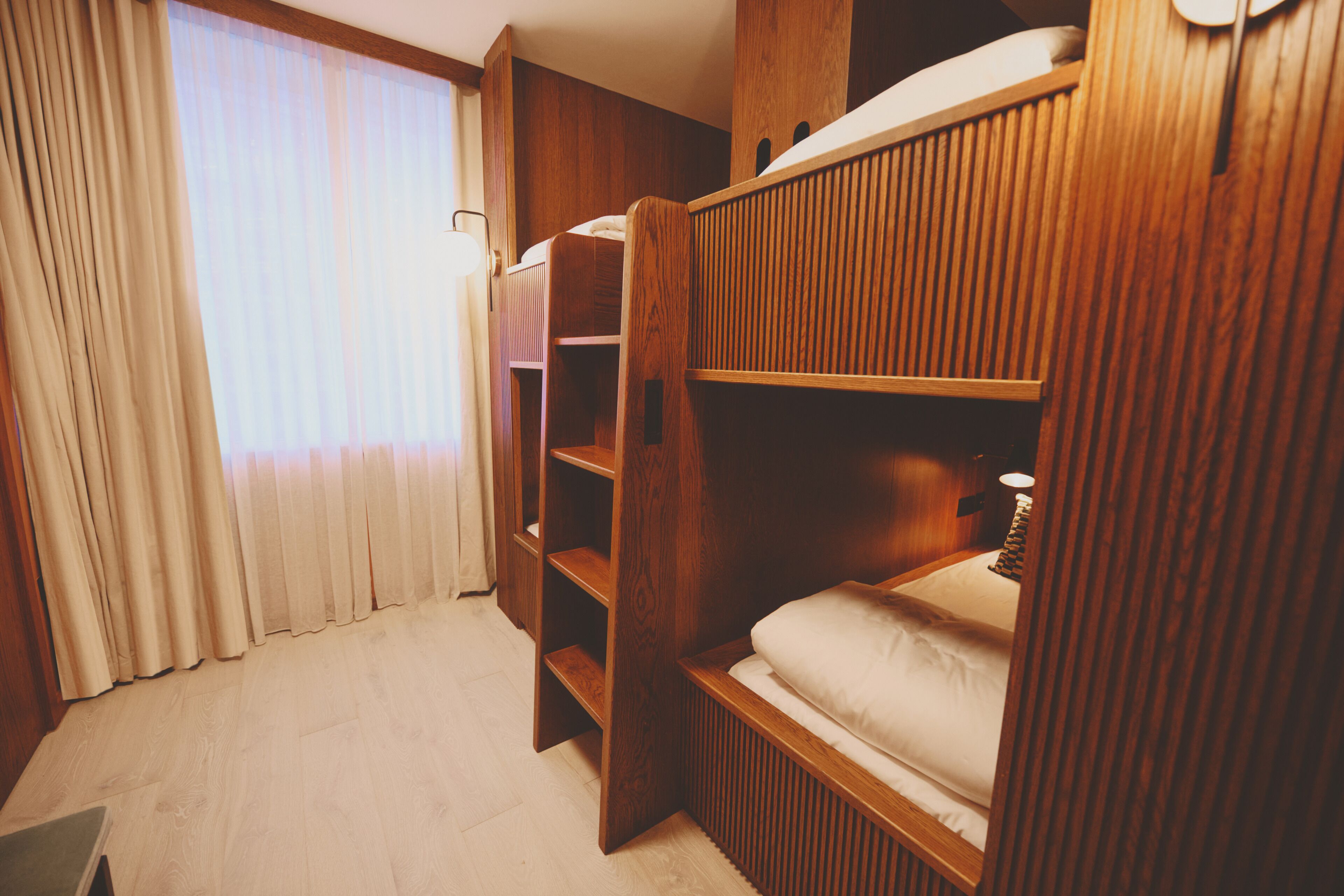 Una camera con un letto a castello, pareti in legno, una finestra con tende e una lampada da comodino.