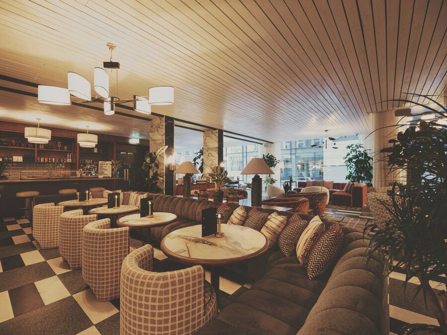 A bar area with checkered flooring, round tables, and bar stools. There are sofas and chairs arranged for seating.