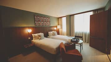 Habitación de hotel con dos camas, una mesita, una silla, un armario y una obra de arte colgada en la pared.