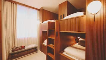 A room with bunk beds, a wooden bench, a tray with a cup and saucer, and a window with curtains.