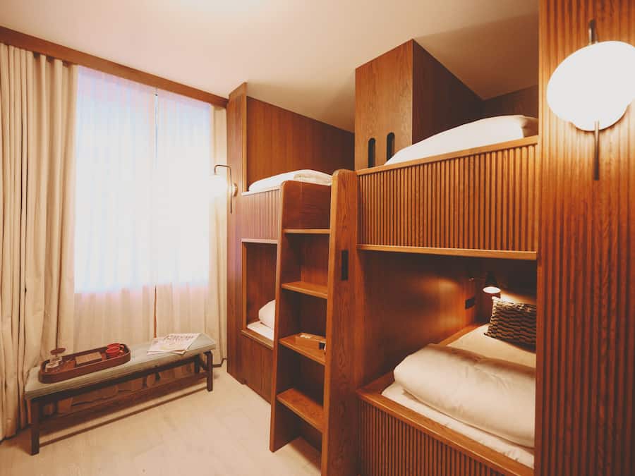 A room with bunk beds, a wooden bench, a tray with a cup and saucer, and a window with curtains.