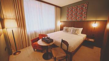 Een hotelkamer met een bed, een stoel, een klein tafeltje met een dienblad, een lamp en een wand met een patroonwandkleed.