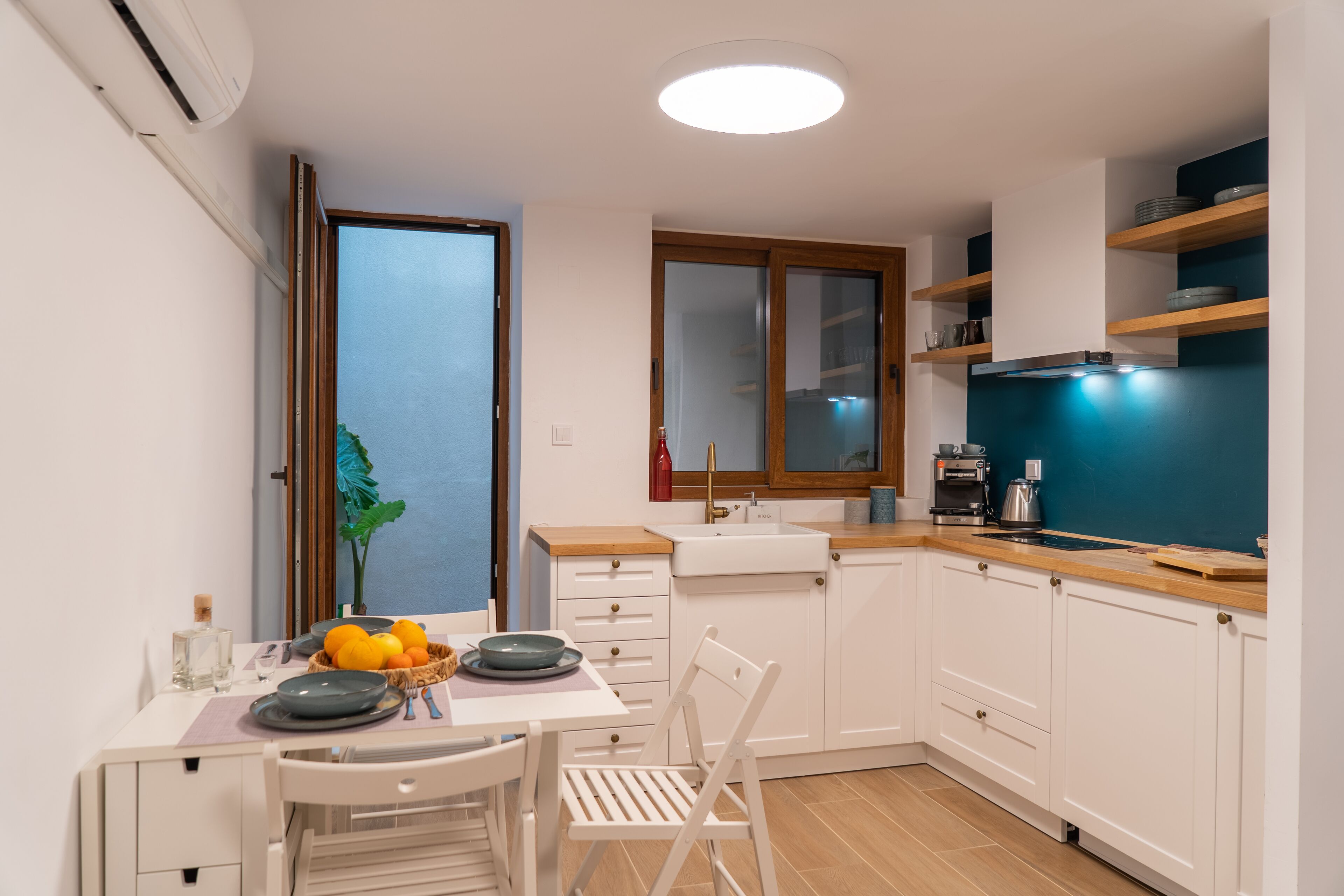 A modern kitchen with white cabinets, a wooden countertop, and a dining area with a table set for two.