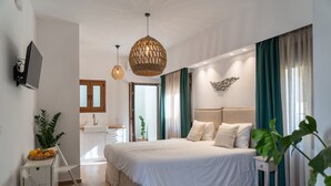 Un dormitorio moderno con una cama grande, mesitas de noche, televisor y una zona de cocina al fondo.