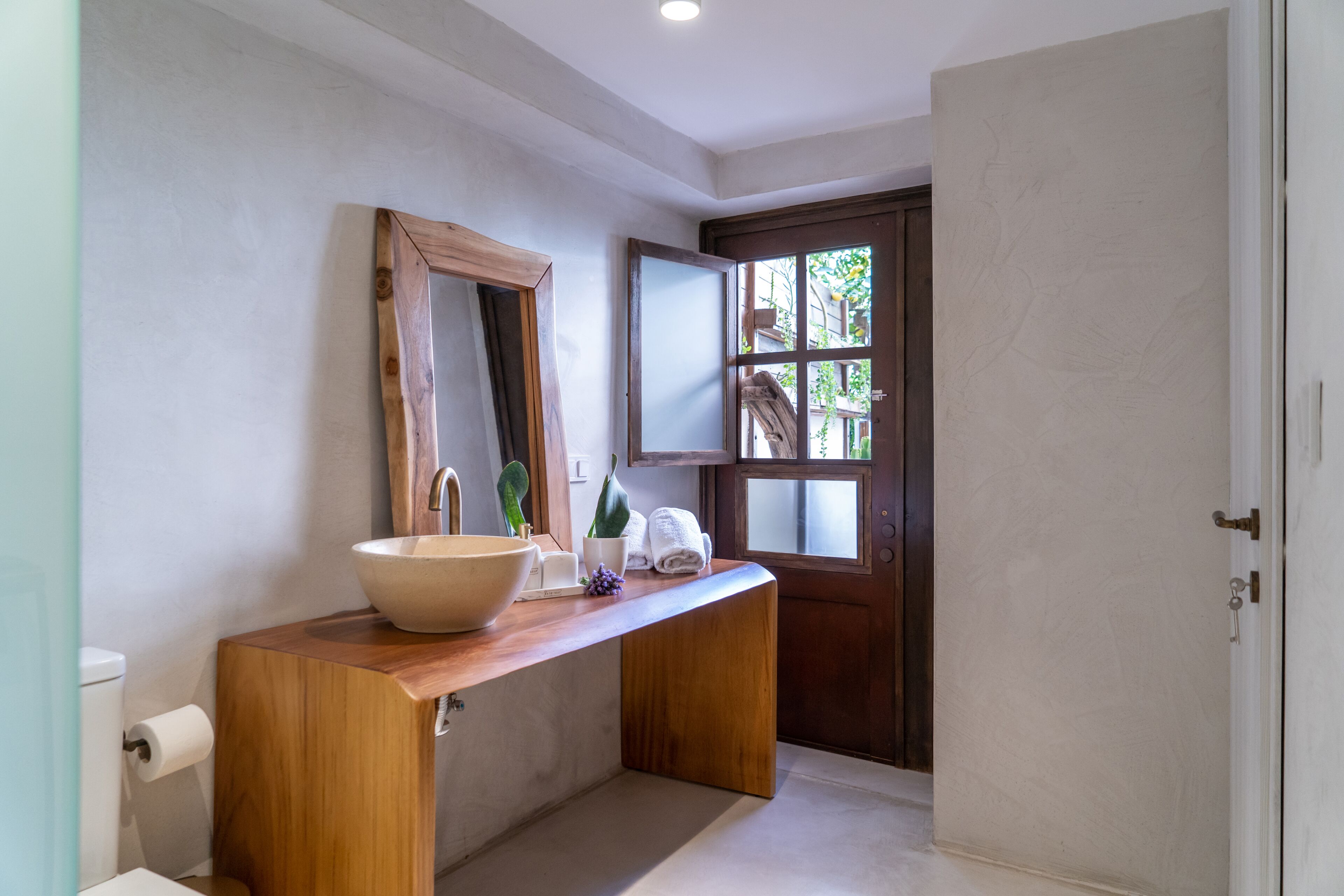A bathroom with a wooden vanity, a large mirror, a sink, and a door leading to a garden.