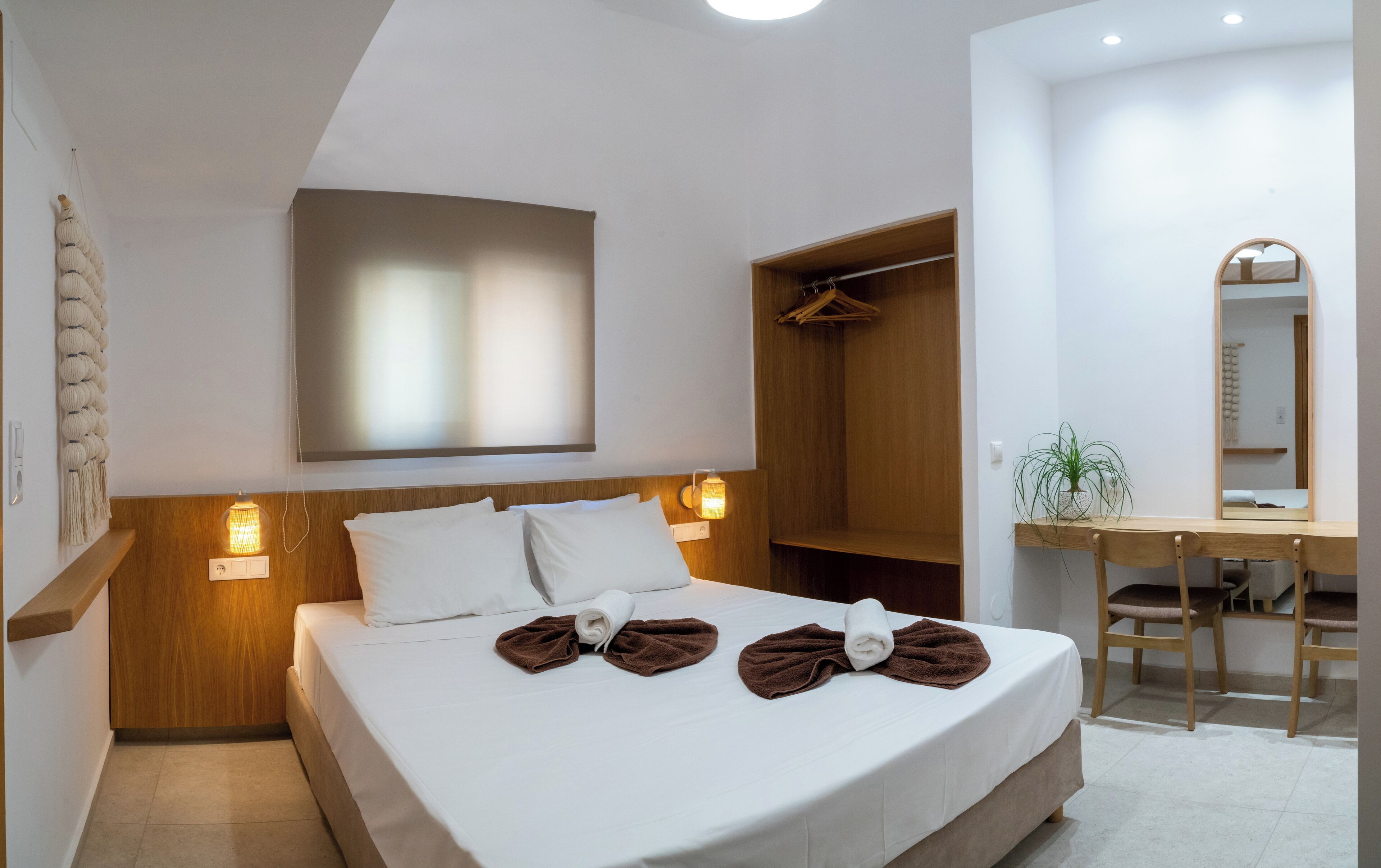A hotel room with a bed, bedside lamps, a wooden wardrobe, a desk, and a mirror.