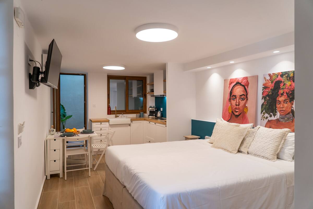 A modern bedroom with a bed, desk, and a TV mounted on the wall.