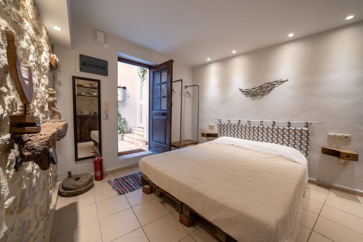 A bedroom with a large bed, a stone wall, a fire extinguisher, and a door leading outside.