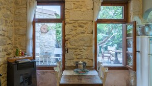 Una habitación rústica con paredes de piedra, una mesa y sillas de madera, un pequeño calentador y vistas al exterior a través de amplios ventanales.