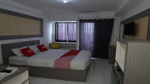 Una habitación de hotel con cama, escritorio, silla, televisión y ventana con cortinas.