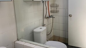 Un baño con azulejos blancos, inodoro, zona de ducha y secamanos.
