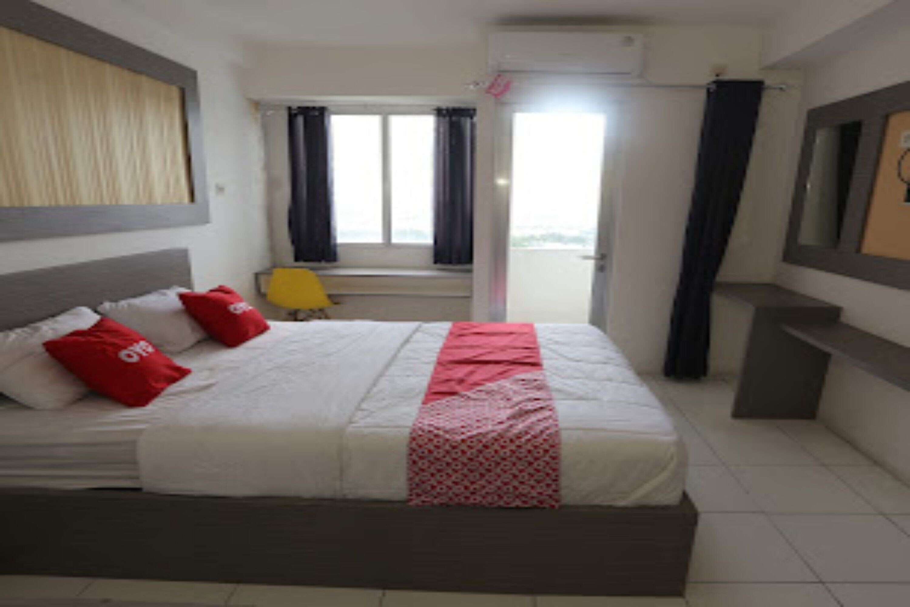Ein Hotelzimmer mit Bett, einem Vorhangfenster, einem kleinen Tisch und einem Spiegel an der Wand.