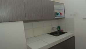 Una cocina con salpicadero de azulejos blancos, un lavamanos de acero inoxidable y un mueble de madera sobre el lavamanos.