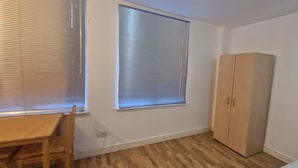 Ein Zimmer mit Holztisch und Stühlen, einem großen Fenster mit Jalousien und einem Kleiderschrank.