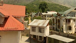 A residential area with houses featuring red and green roofs, surrounded by lush green hills. - Silver Oak (Srinagar)
