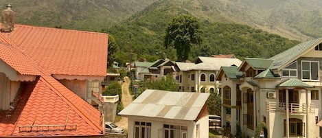 A residential area with houses featuring red and green roofs, surrounded by lush green hills.