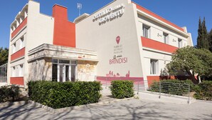 A building with a red and white facade, a sign reading "OSTELO NELL' ALCOVA DI GIOVENTU," and a "POP BRINDISI" marker.