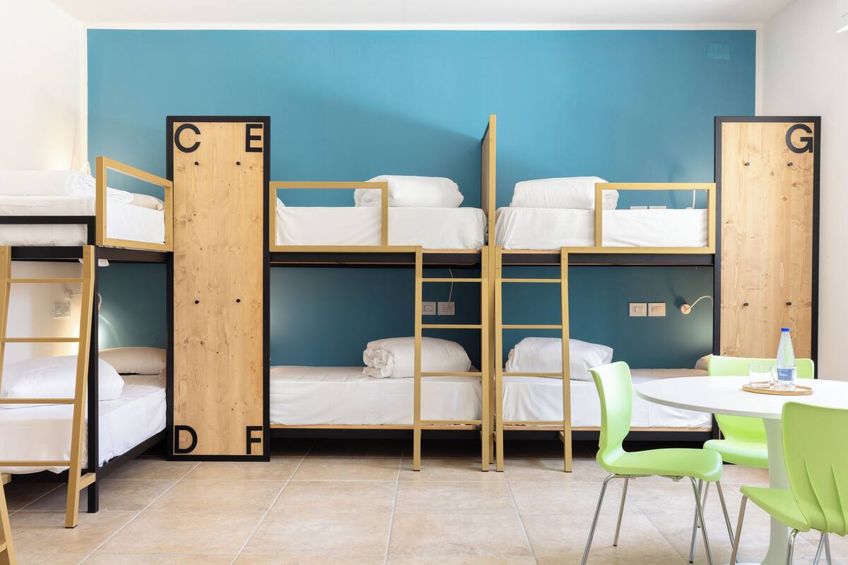 A dormitory room with bunk beds, a small table with chairs, and a blue wall.