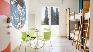 A compact room with a dining table and chairs, a bunk bed, and a large window with a view of trees.