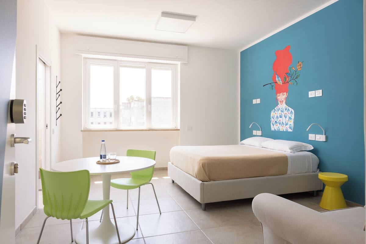 A modern bedroom with a bed, a green chair, a white table, and a yellow side table.