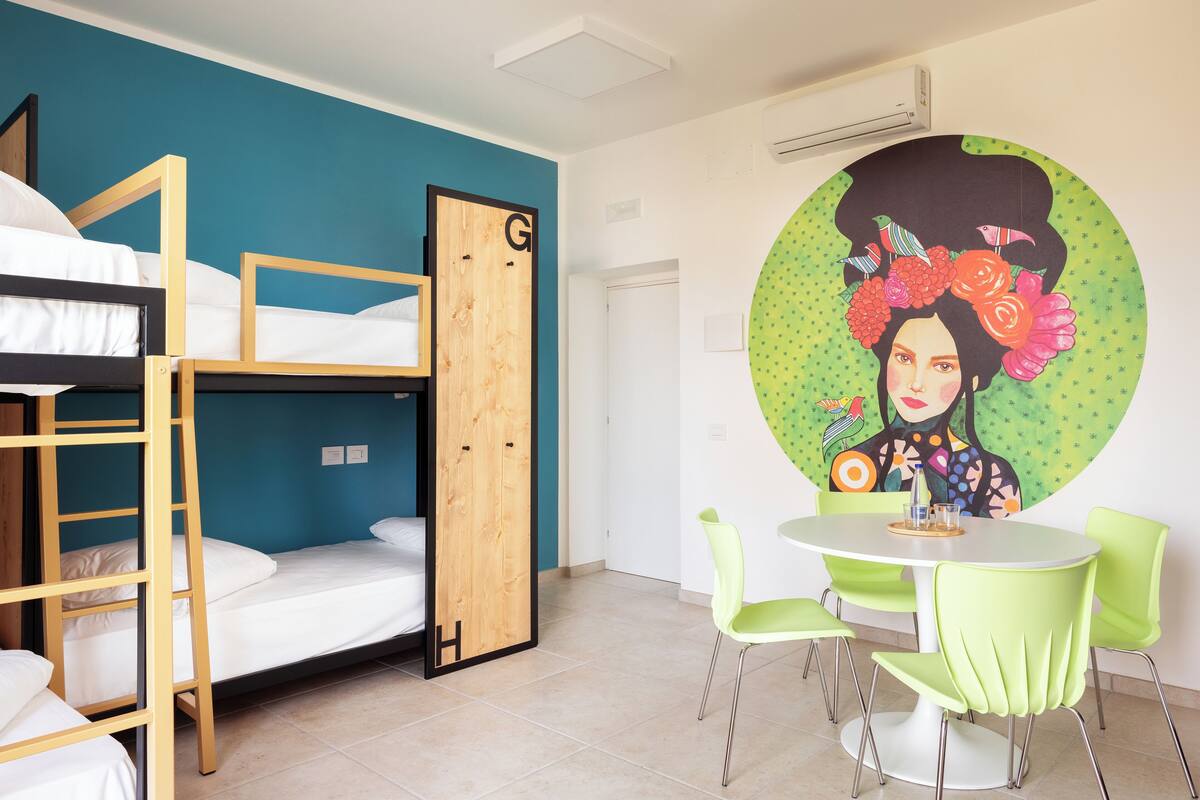 A dormitory room with bunk beds, a round table with chairs, and a wall mural.