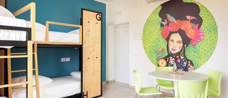 A dormitory room with bunk beds, a round table with chairs, and a wall mural.