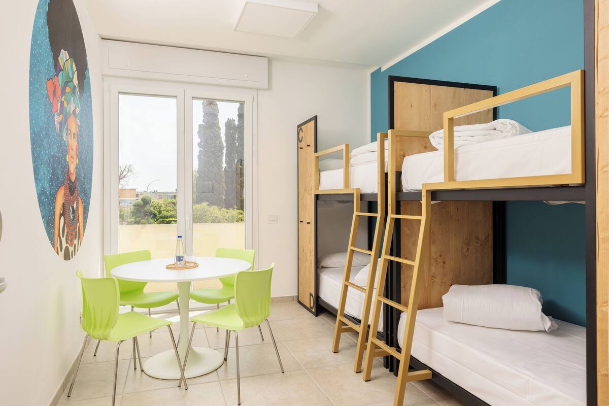 A room with bunk beds, a round table with chairs, and a painting on the wall.
