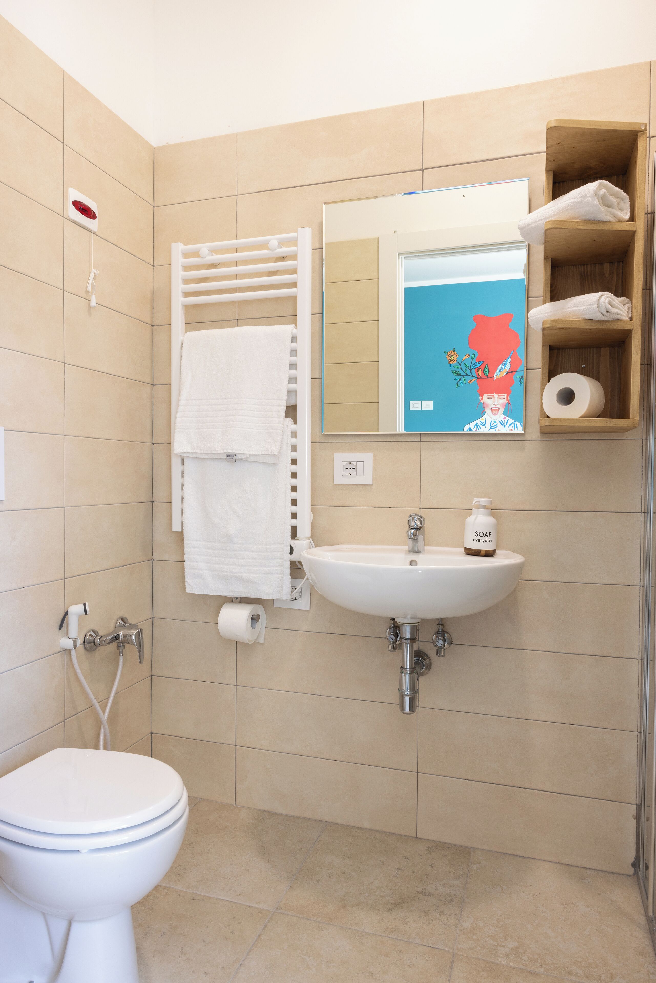 Une salle de bain comprenant des toilettes, un lavabo, un porte-serviettes et une étagère avec des serviettes et un distributeur de savon.
