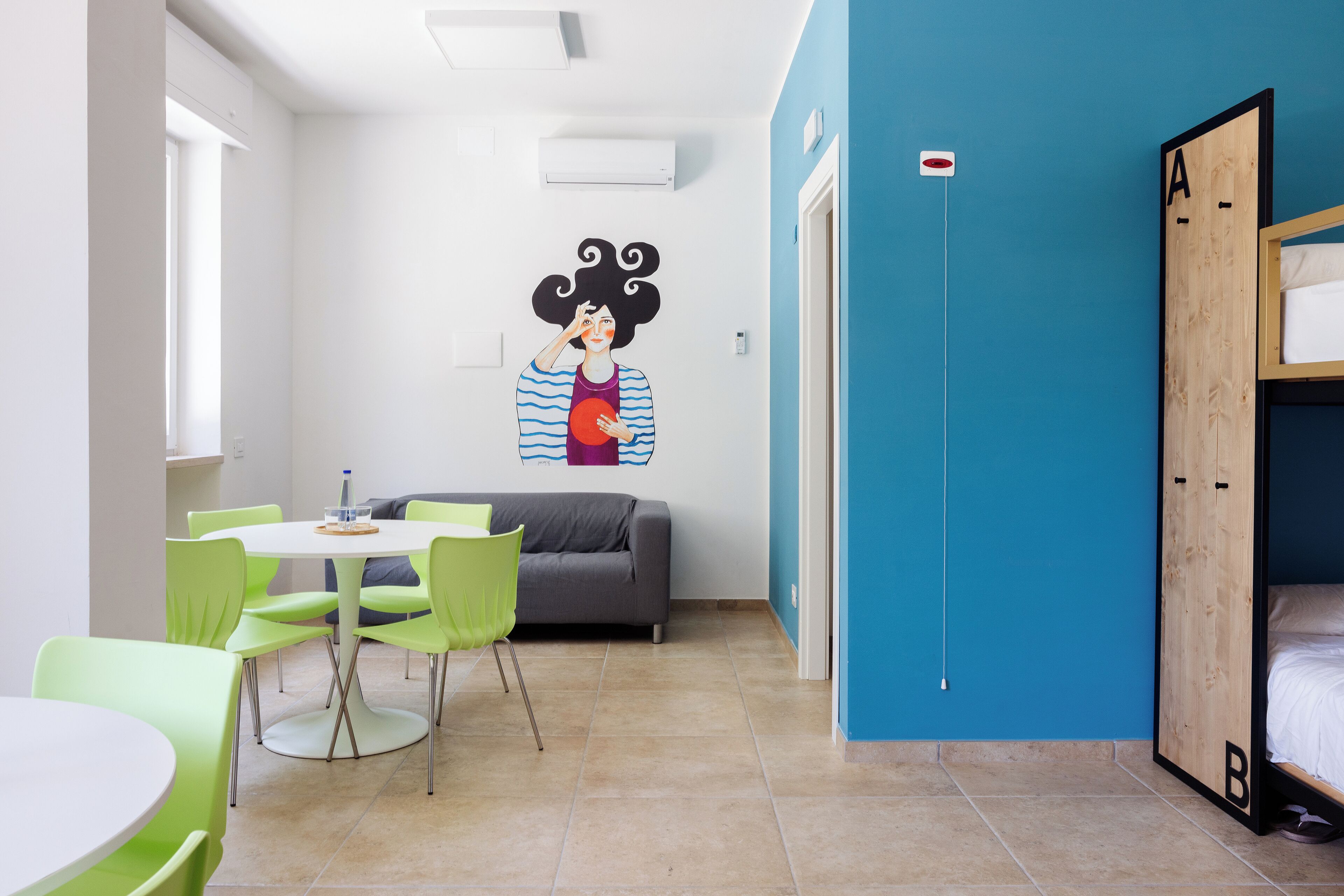 A room with a bunk bed, a dining table with chairs, a sofa, and a wall mural.
