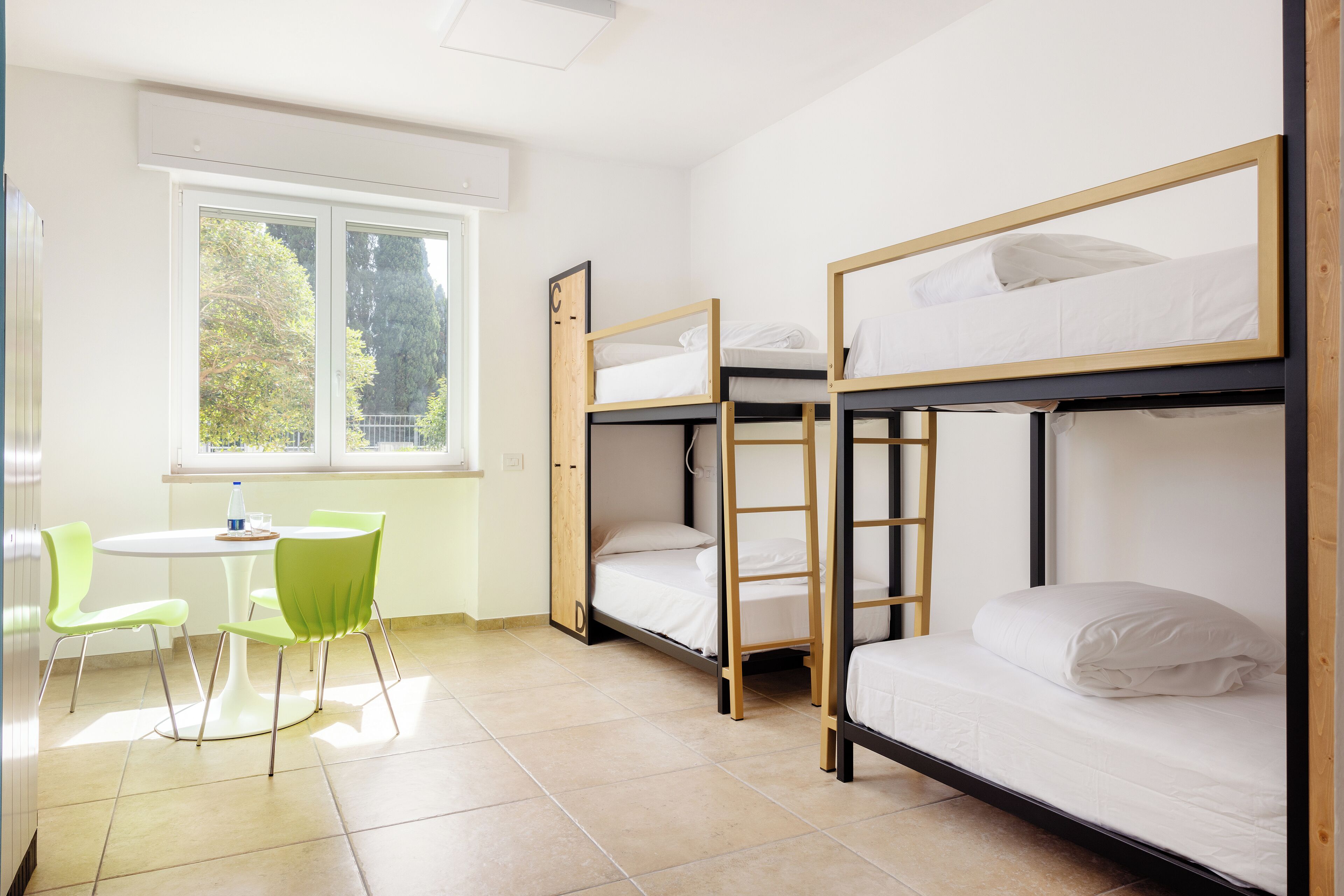 Un dormitorio con literas, una mesita pequeña y dos sillas verdes.