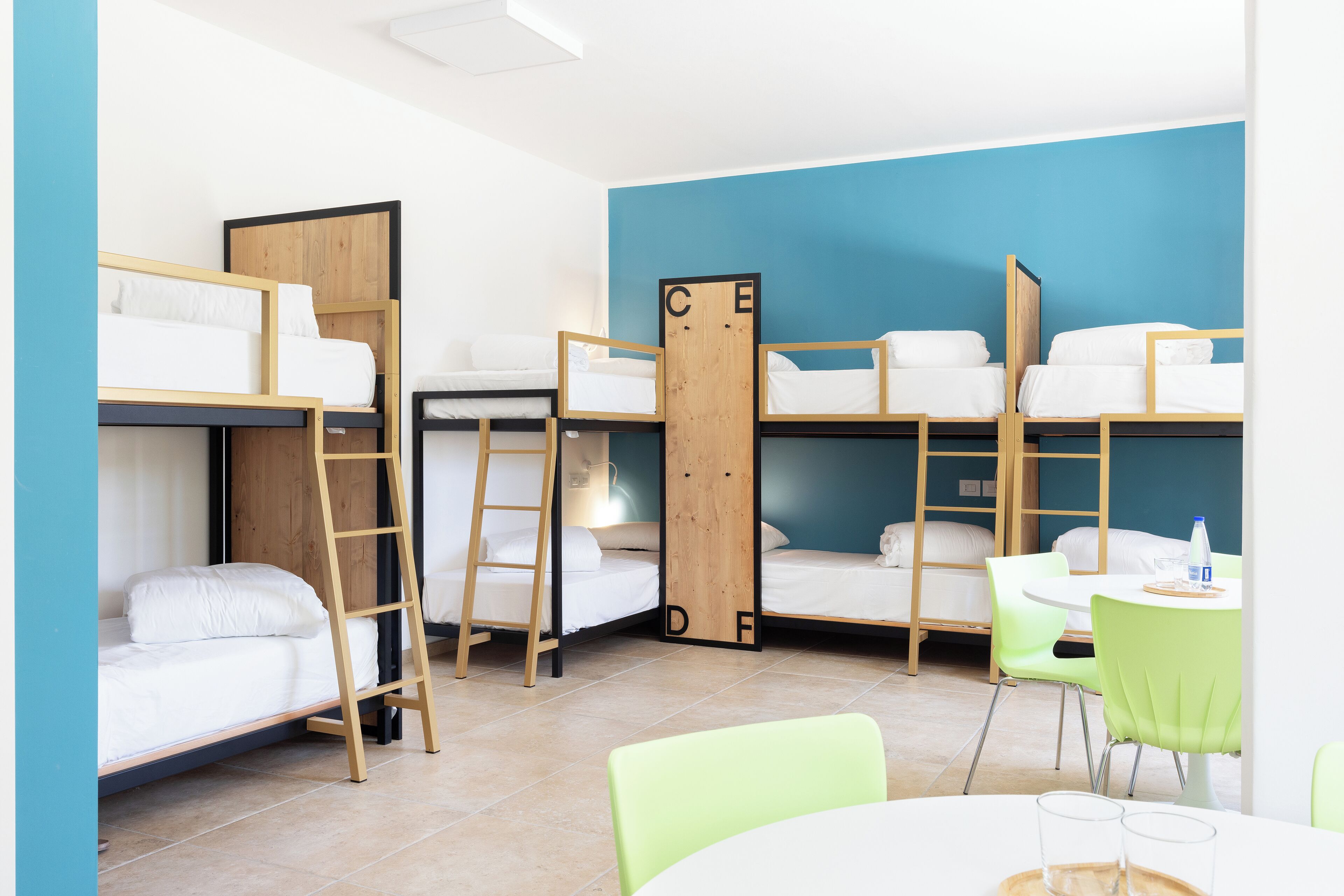 A dormitory room with bunk beds, a ladder, a desk, and a chair.