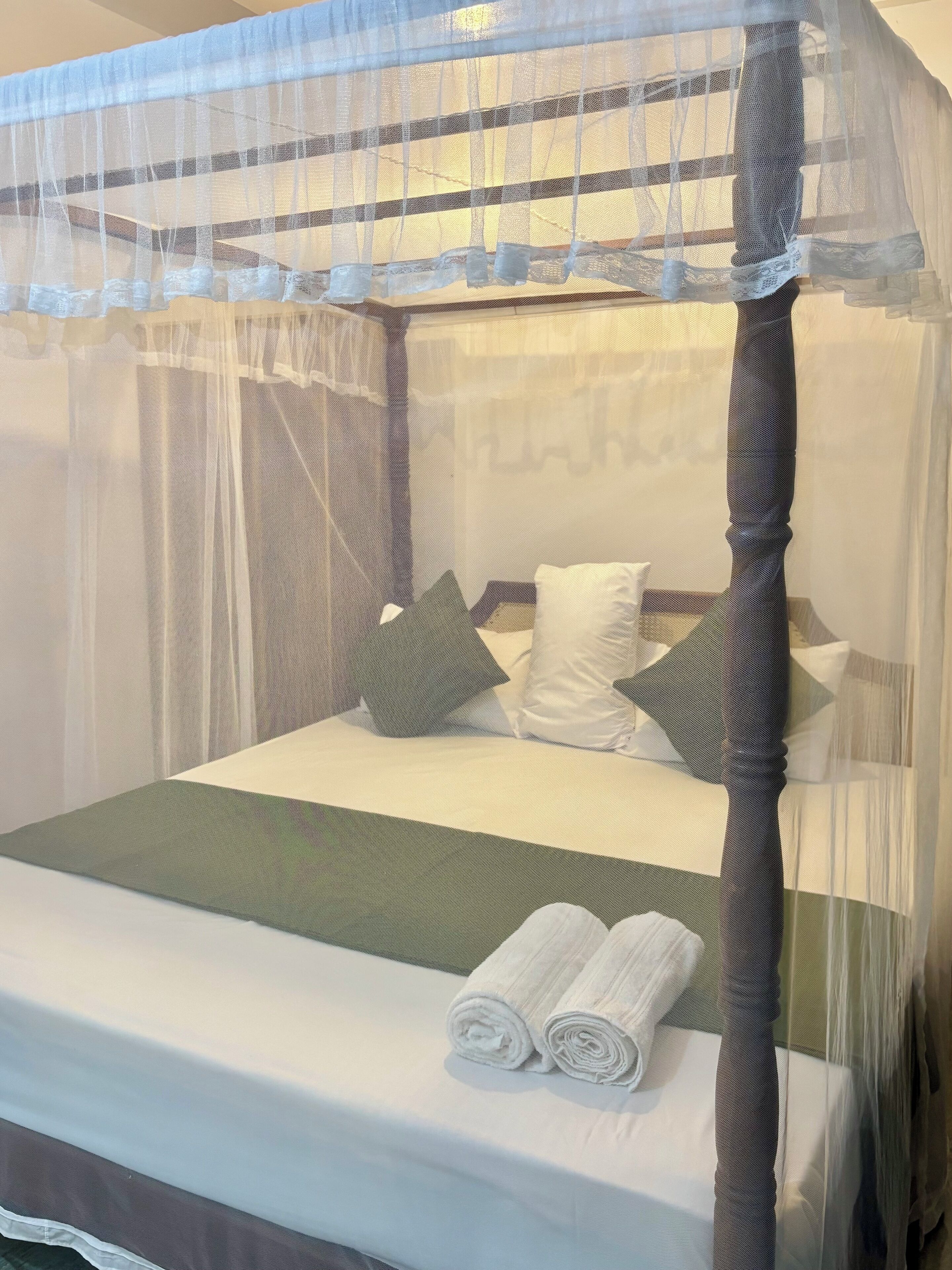 A bed with a canopy, pillows, and rolled towels.