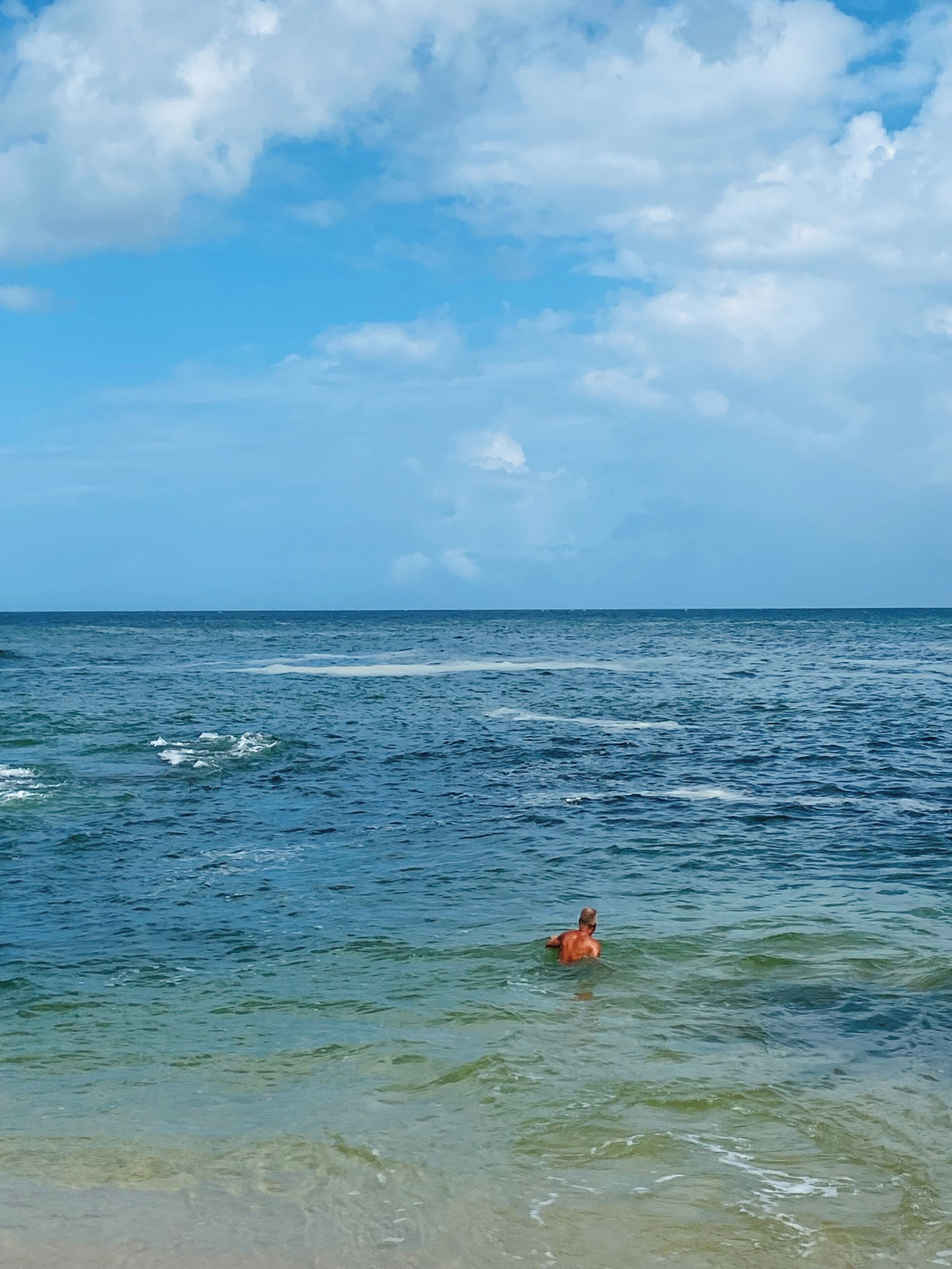 A beach with clear water and a person swimming.