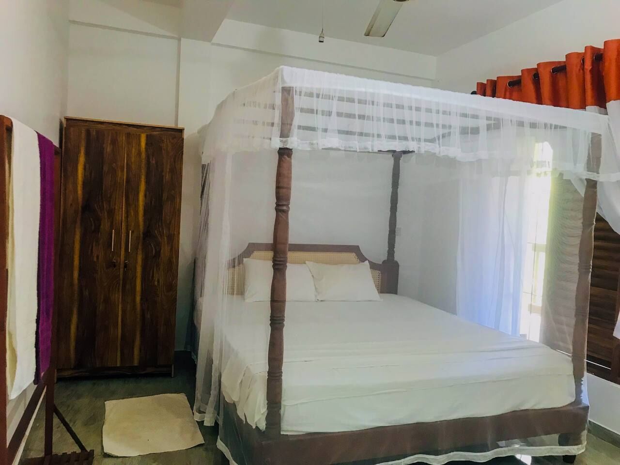 A four-poster bed with a canopy, a wooden wardrobe, and a small rug on the floor.