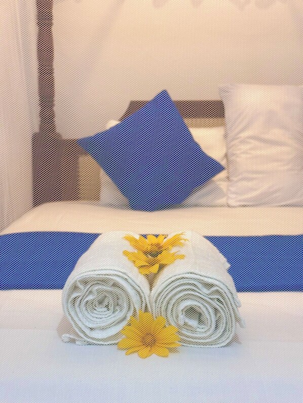 A neatly made bed with a blue pillow, white bedding, and a decorative towel with yellow flowers.