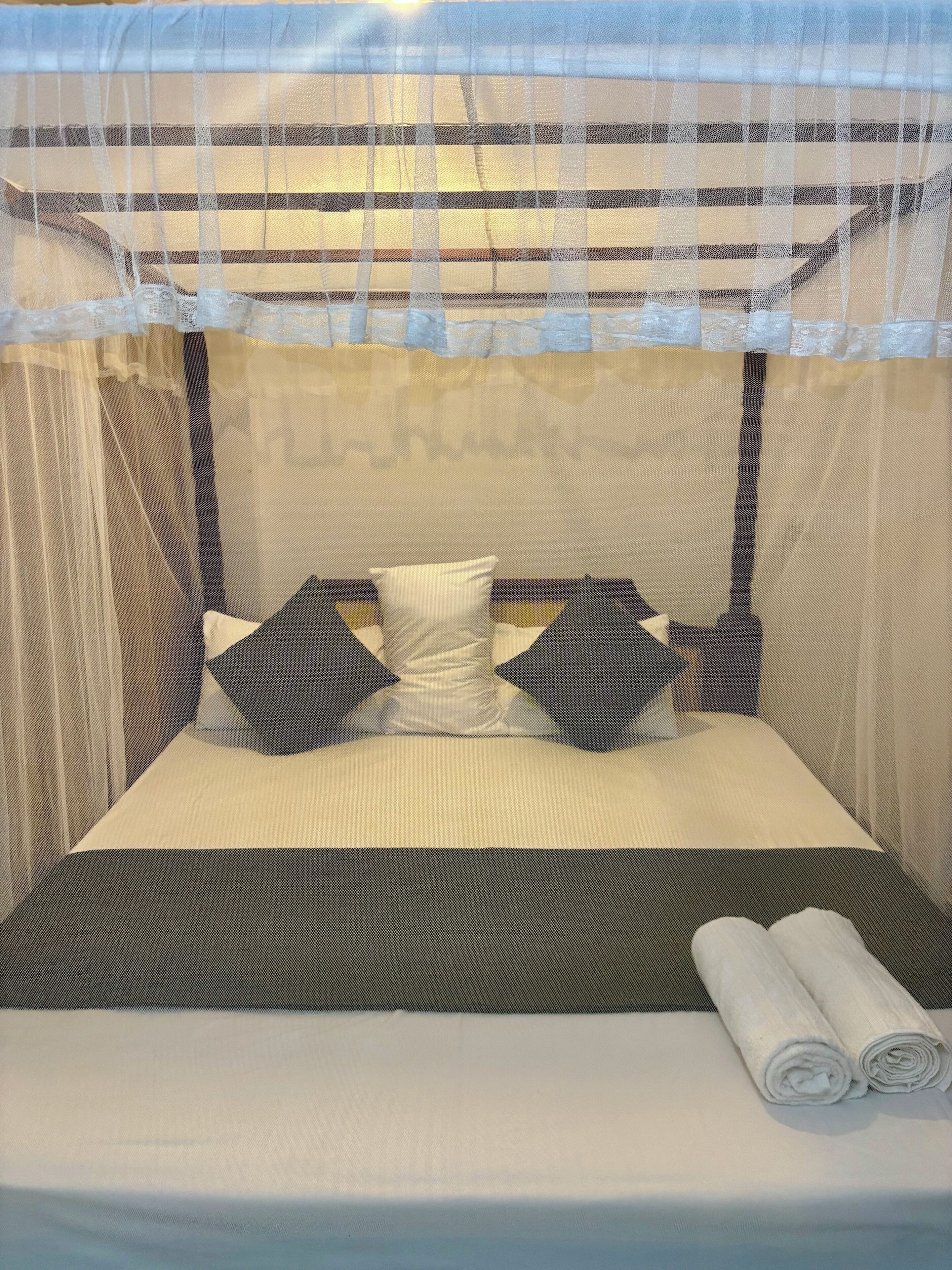 A bed with a canopy, pillows, and a rolled towel.