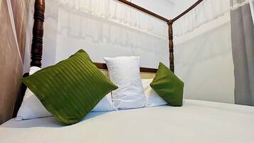 Una cama con ropa de cama blanca, almohadillas verdes y cortinas traslúcidas, con cabecera de madera.