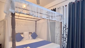 Ein Himmelbett mit Baldachin, ein Deckenventilator und ein Bett mit blauer Bettdecke und weißen Kissen.