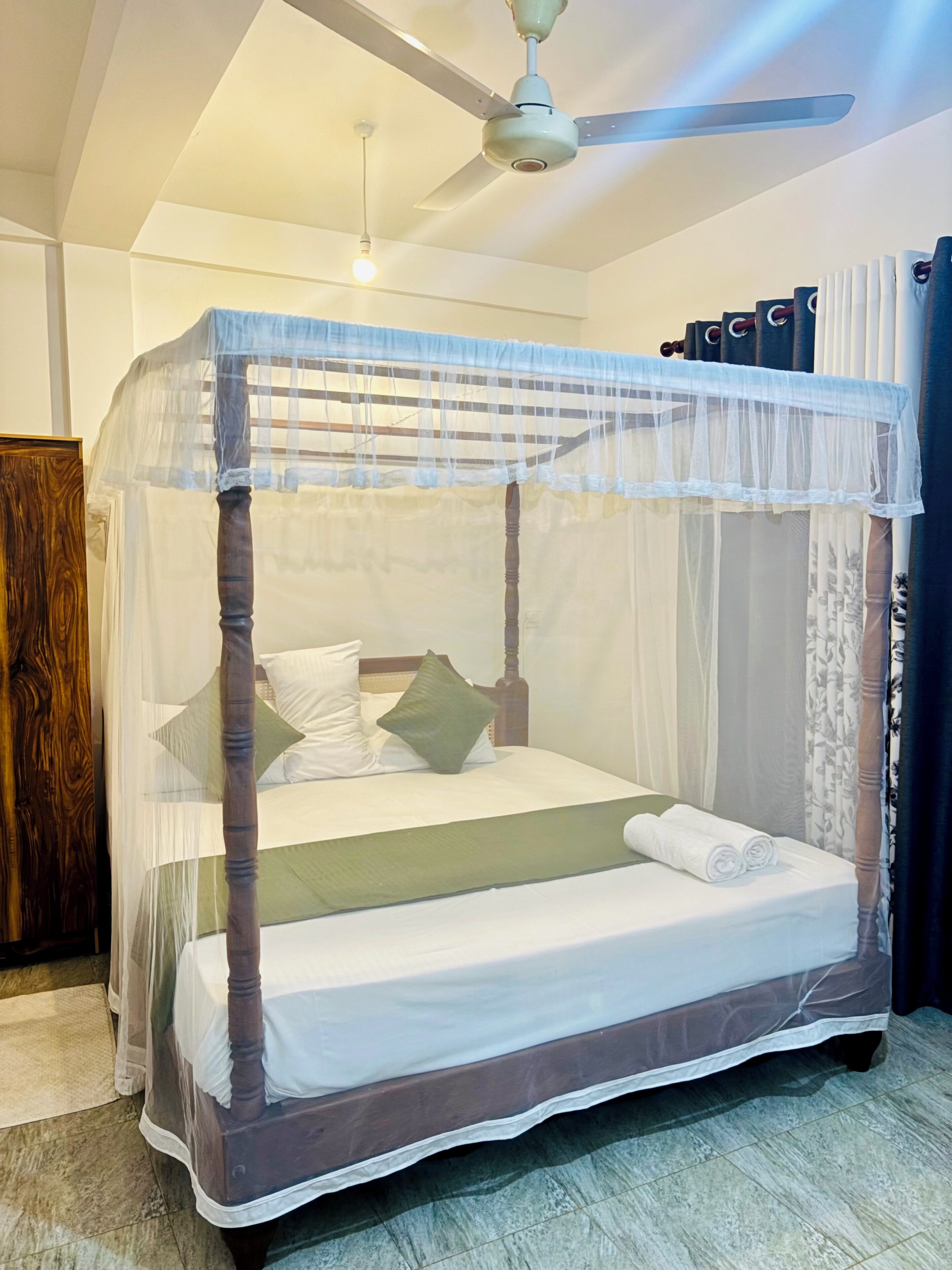 Una cama con dosel, un ventilador de techo y una mesita de noche.